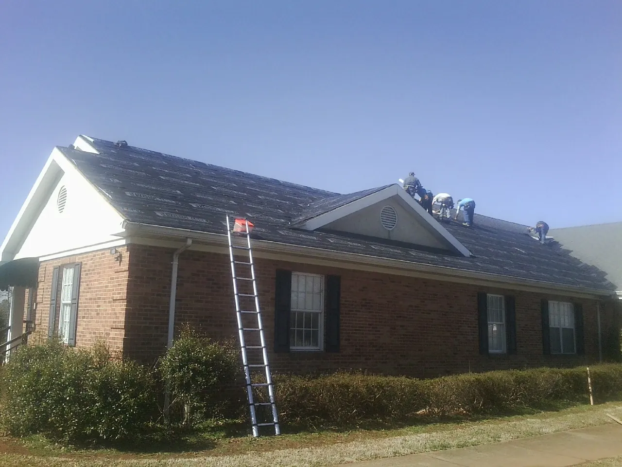 Crew tearing shingles off a brick ranch roof with a ladder set — Emergency Roof Repair work by our crew in Chadds Ford
