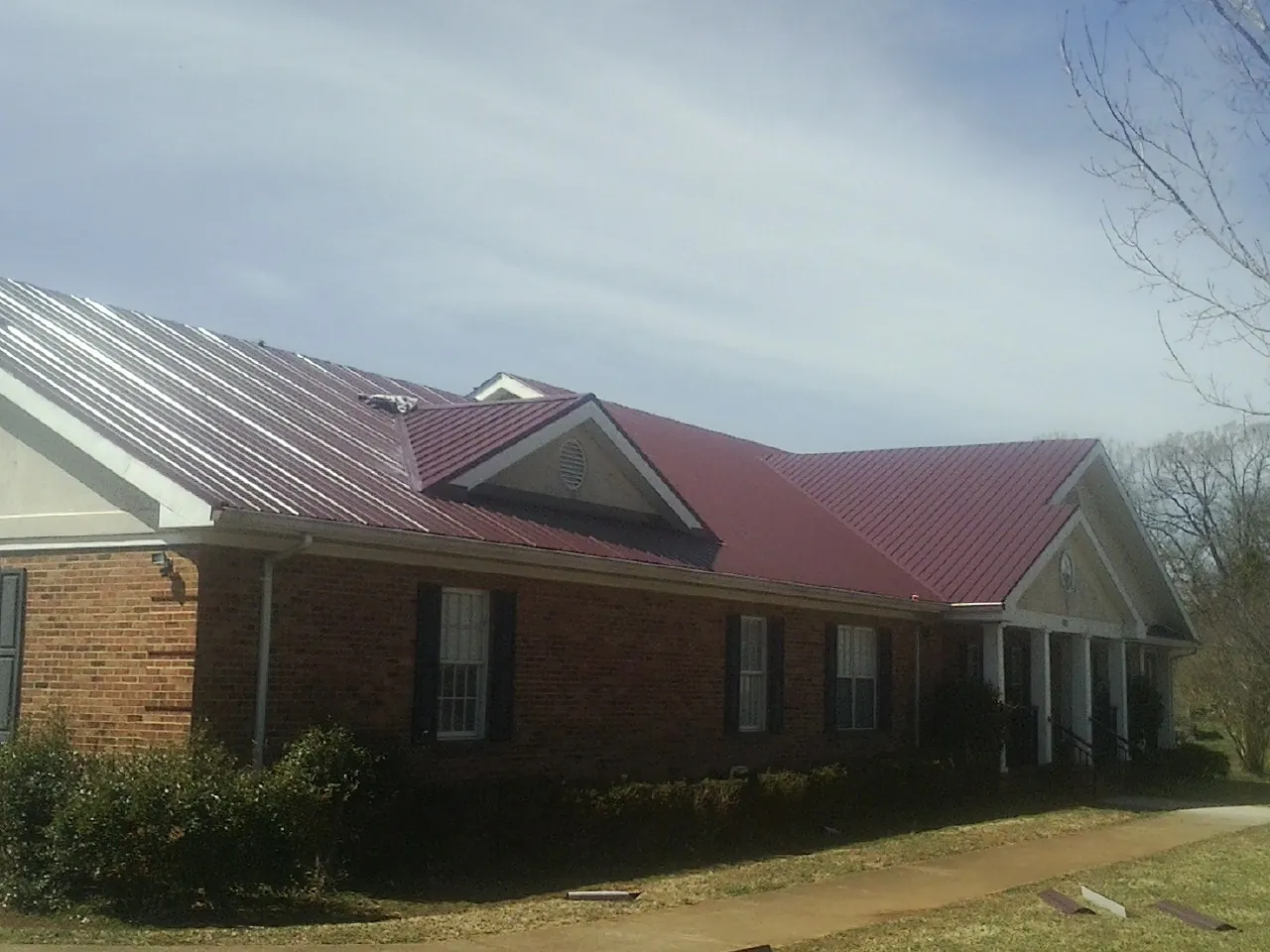 Red metal roof with gabled entries on a long brick building, from a Hail Damage Roof Repair job in Chadds Ford