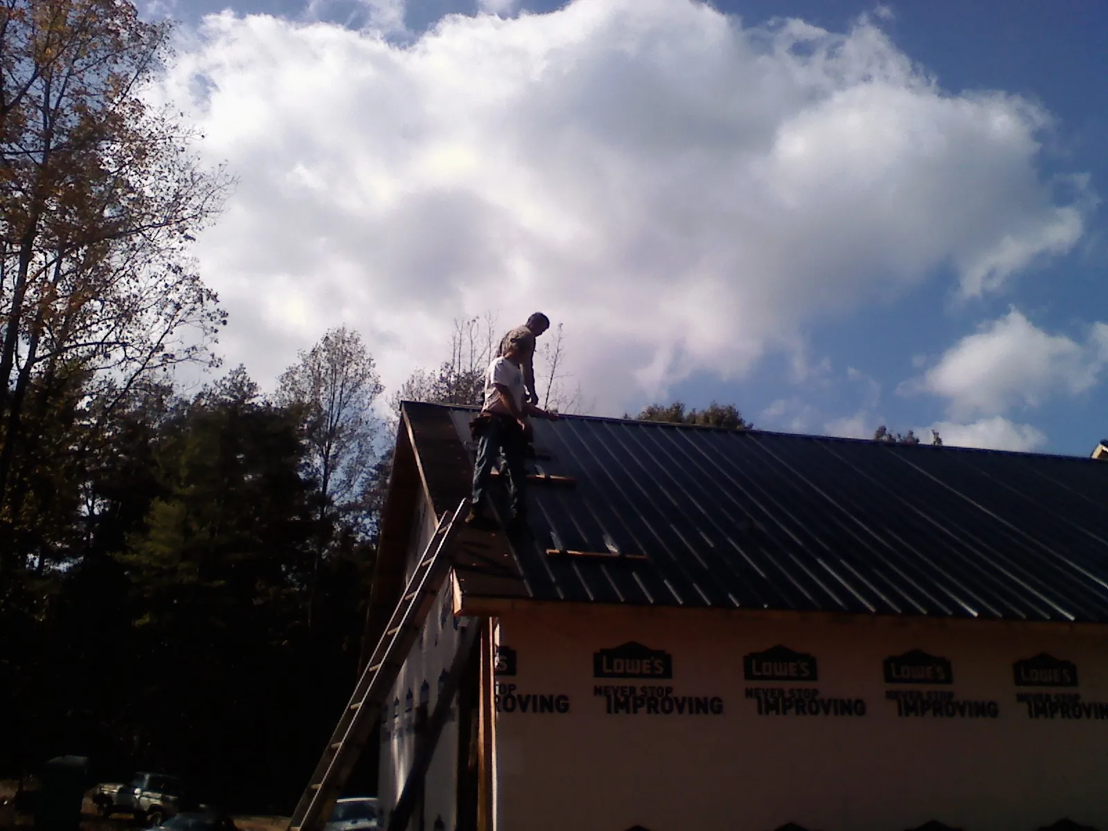 Roofer fastening dark metal panels high against a cloudy sky, from a Roof Inspection job in Chadds Ford