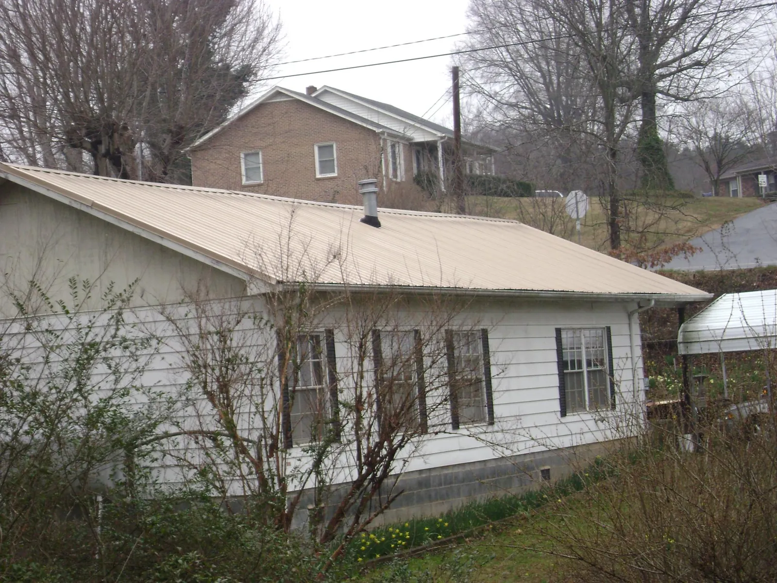 Tan metal roof on a white sided house set into a hillside — Commercial Roofing by Roofing Brothers in Chadds Ford